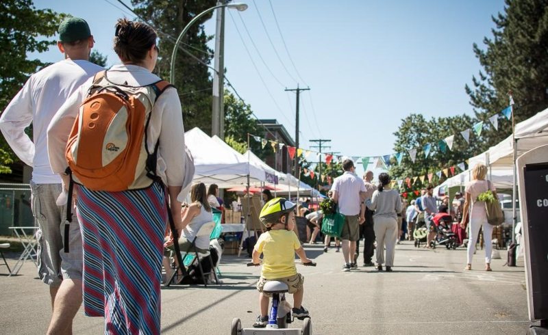 A low-angle shot of a farmers market. In the frame, a kid is riding a tricycle in the Ski Run Farmers Market
